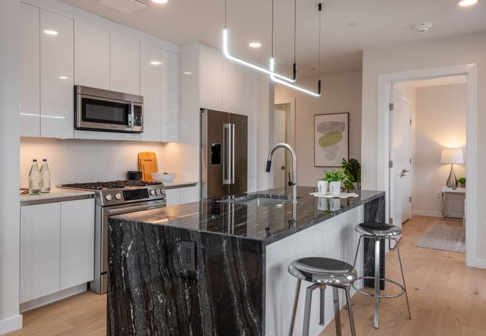 Well-lit kitchen with a dark marbled countertop, white cabinets, and a view of an adjacent room.
